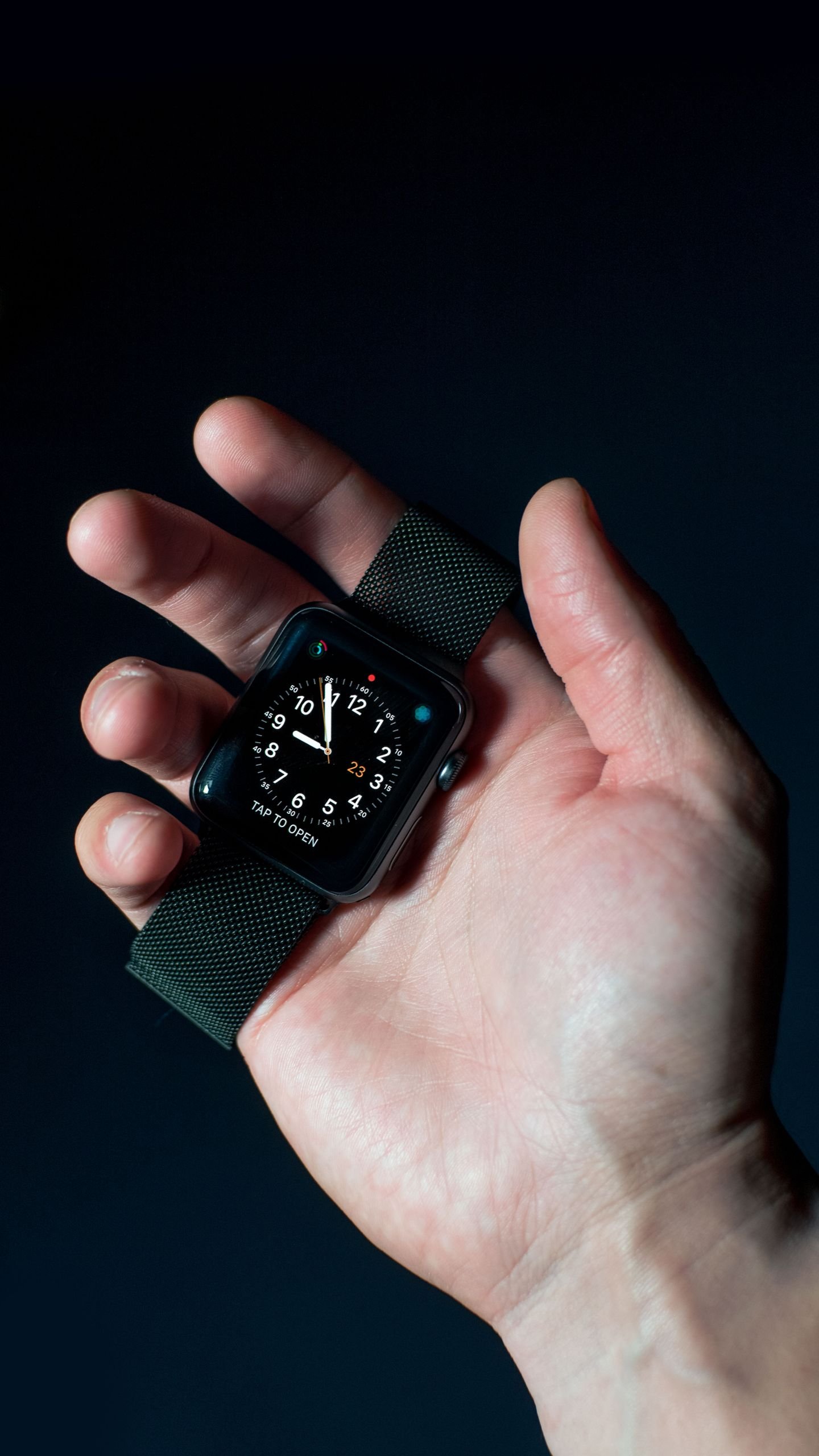 Close-up of a hand holding a smartwatch with an analog time display against a dark background.