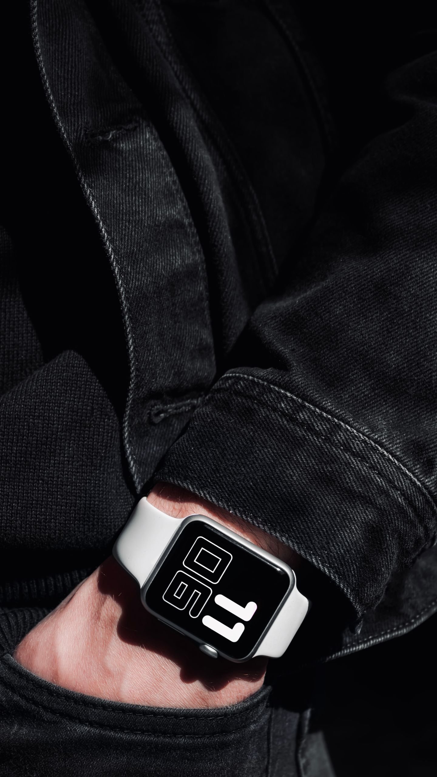 Close-up shot of a hand wearing a smartwatch with a bold digital display, paired with a denim jacket.