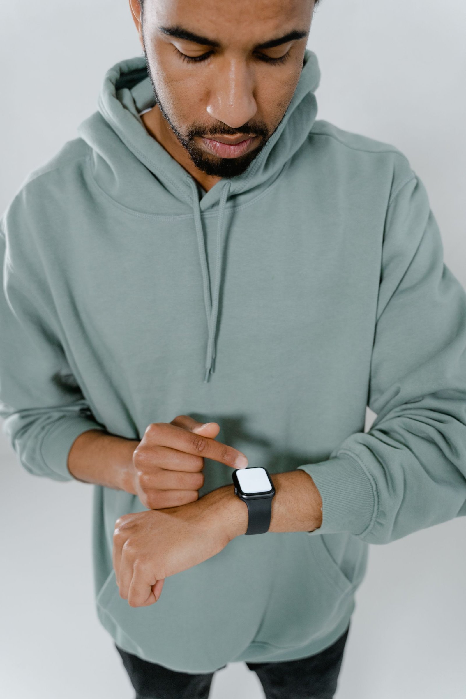 Man wearing a green hoodie checking time on a smartwatch, emphasizing modern technology.