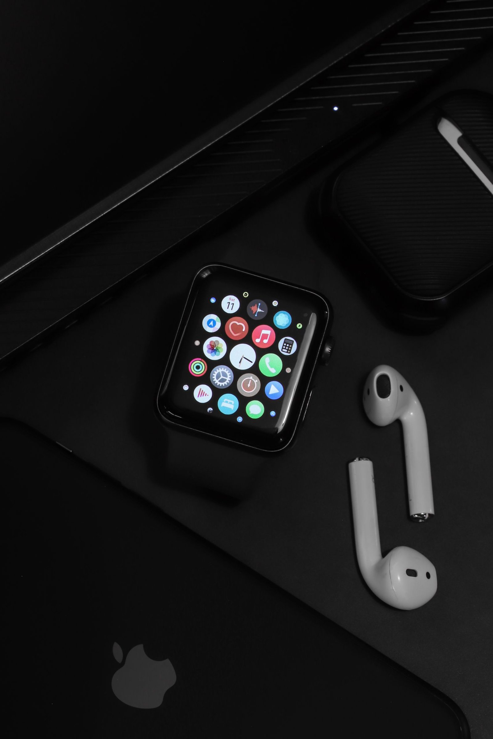 Stylish arrangement of modern tech gadgets on a dark surface, showcasing an Apple watch and AirPods.