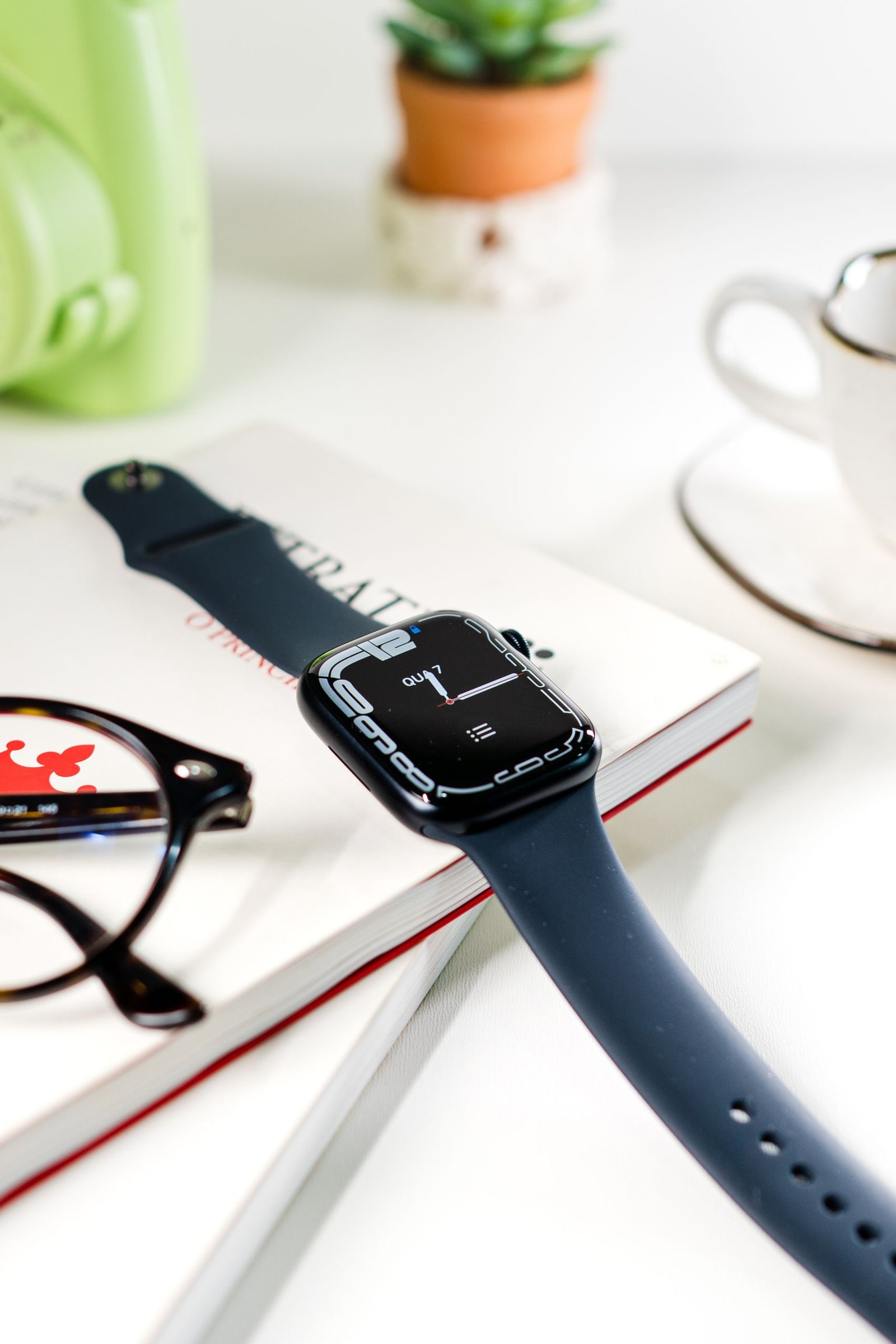 Stylish smart watch displayed on a desk with books and glasses, showcasing modern technology and lifestyle.