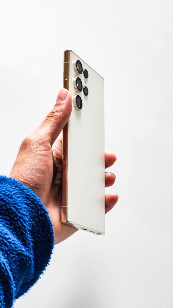 A hand holding a sleek white smartphone with multiple rear cameras, showcasing modern technology.