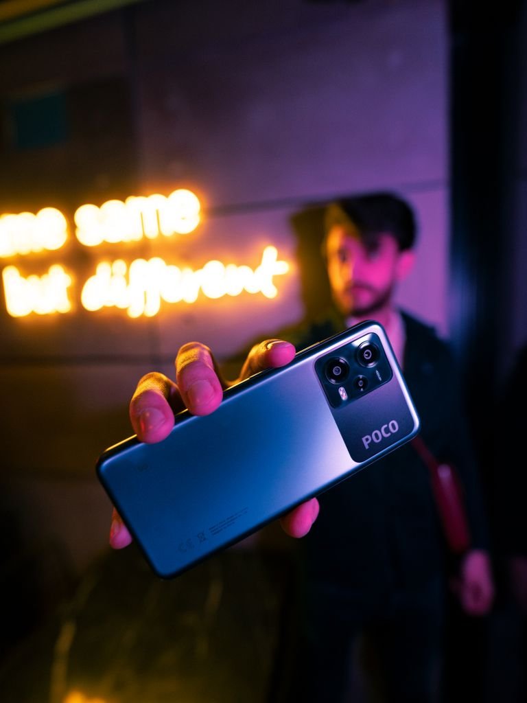 A person holds a smartphone with neon signs glowing in the background, creating a vibrant urban feel.