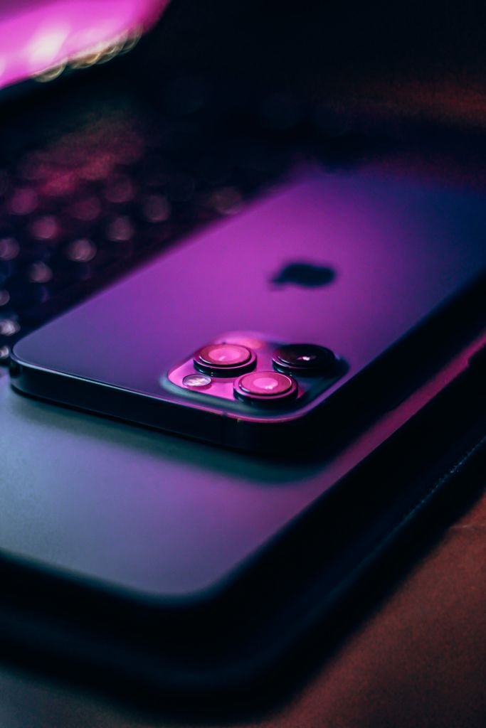 Close-up of a modern smartphone with glowing pink-blue tones on a dark surface.