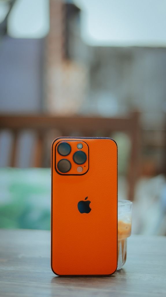 Vibrant orange smartphone with triple camera setup on a table outdoors.