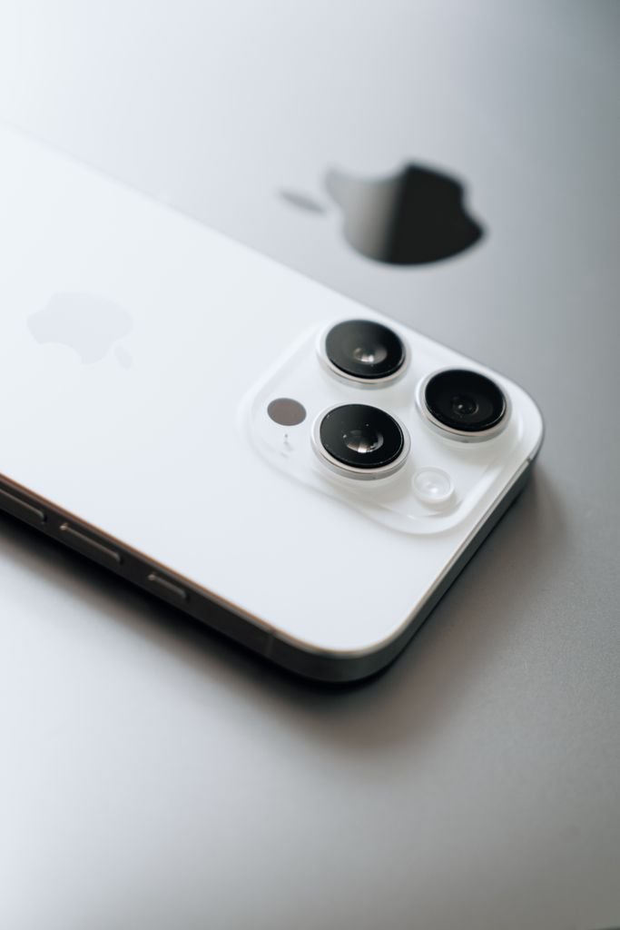 White smartphone with triple cameras lies atop a sleek laptop.